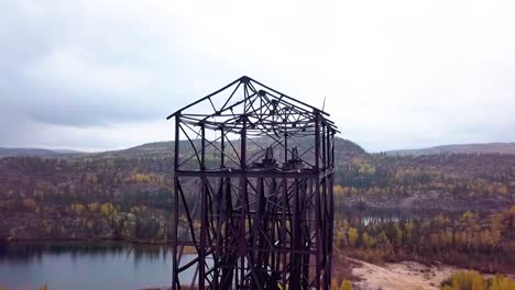 slow-motion aerial-orbit panning shot of an abandoned mine headframe in the boreal forest in the fall