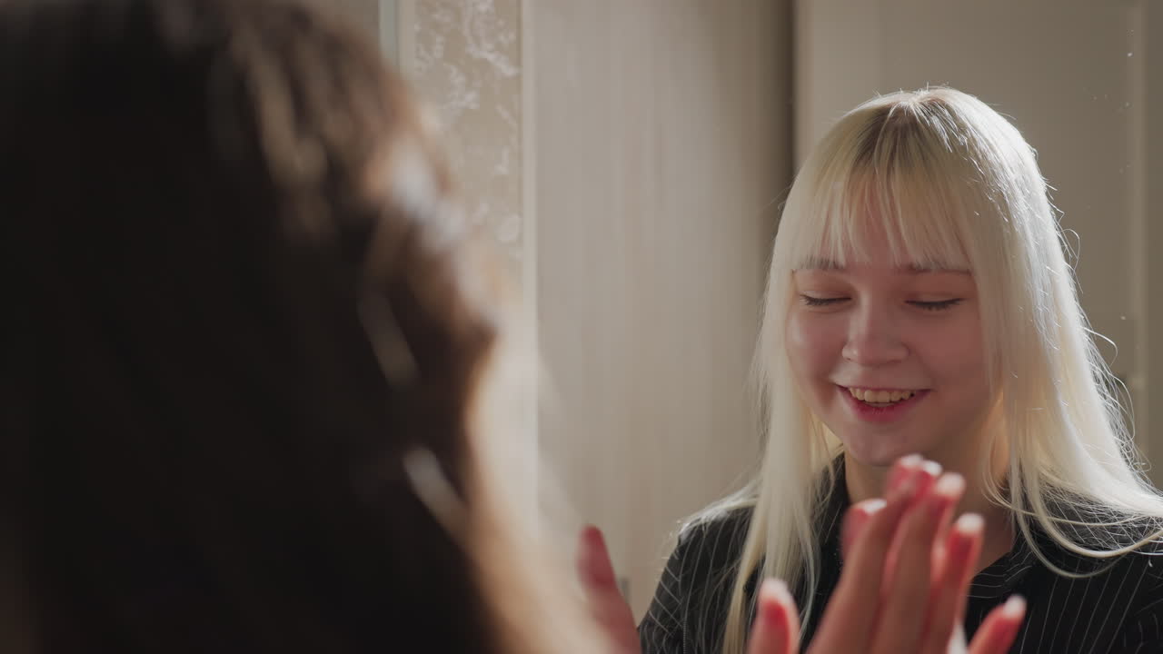 rear view of girl and sister clapping hands together in apartment hallway near kitchen cabinets, light casting soft glow on blonde hair, capturing playful sibling bonding moment indoors