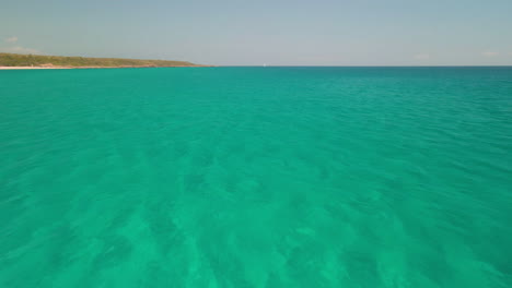 Volando-Sobre-Un-Hermoso-Mar-Tropical-Con-Velero-Y-Costa-En-Segundo-Plano-En-Cerdeña,-Italia---Toma-Aérea-De-Drones