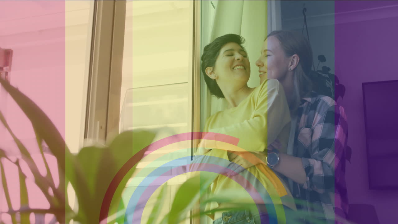 animación del orgullo bandera arco iris y anillos sobre feliz pareja de lesbianas caucásicas abrazándose en casa