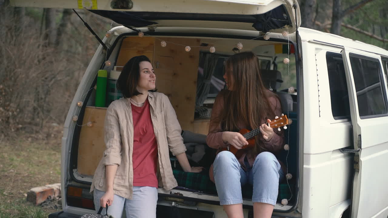 두 명의 어린 여자 친구가 숲 한가운데 캐러밴 뒤에서 수다를 떨다 1