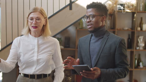 diverse male and female colleagues walking with tablet and speaking