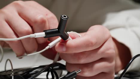 Young woman trying to untangle the headphones close-up. Special adapter for headphone. Tangled wires on table. Trying to untangle many messy cables