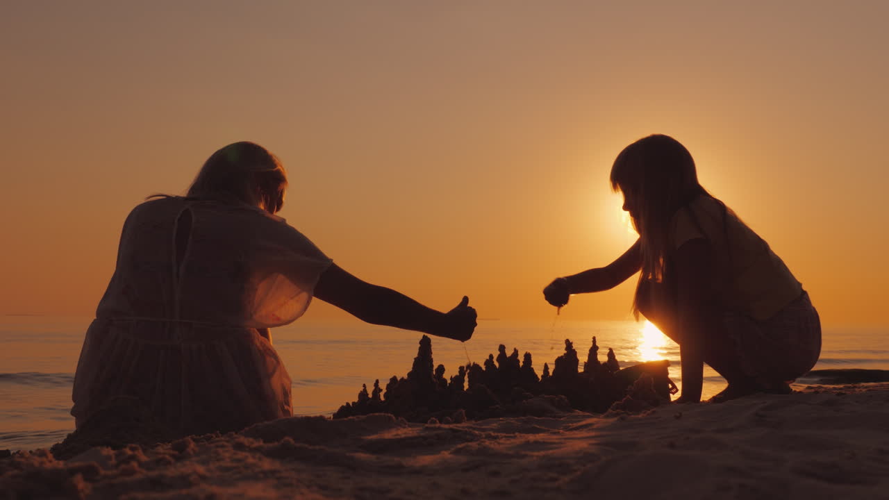 어머니는 해변에서 딸과 함께 놀며 모래 4k 비디오로 만든 성을 짓습니다.