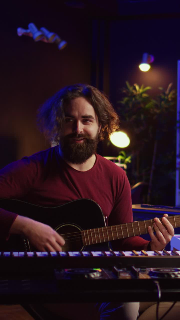 Uomo barbuto che suona la chitarra acustica e sorride in uno studio musicale
