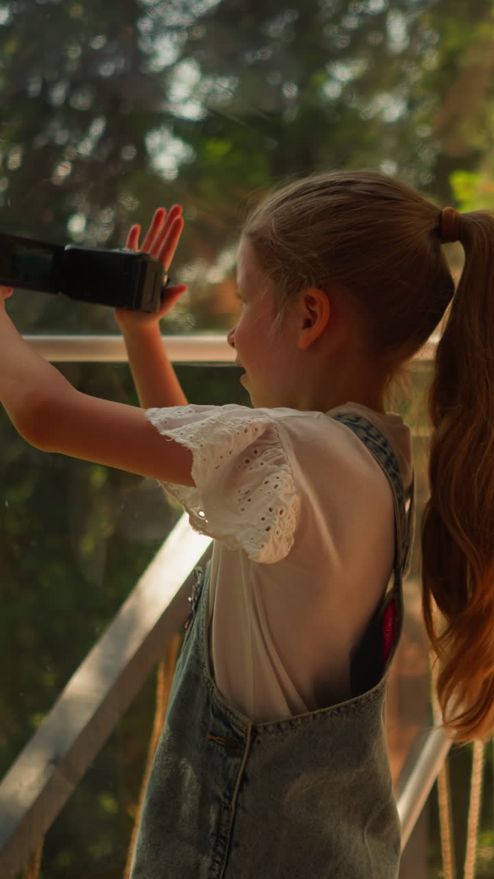 niño dispara en el lago del bosque en glamping. niña pequeña concentrada toma video de bosque salvaje en un hotel ecológico. niño con cámara digital en vacaciones