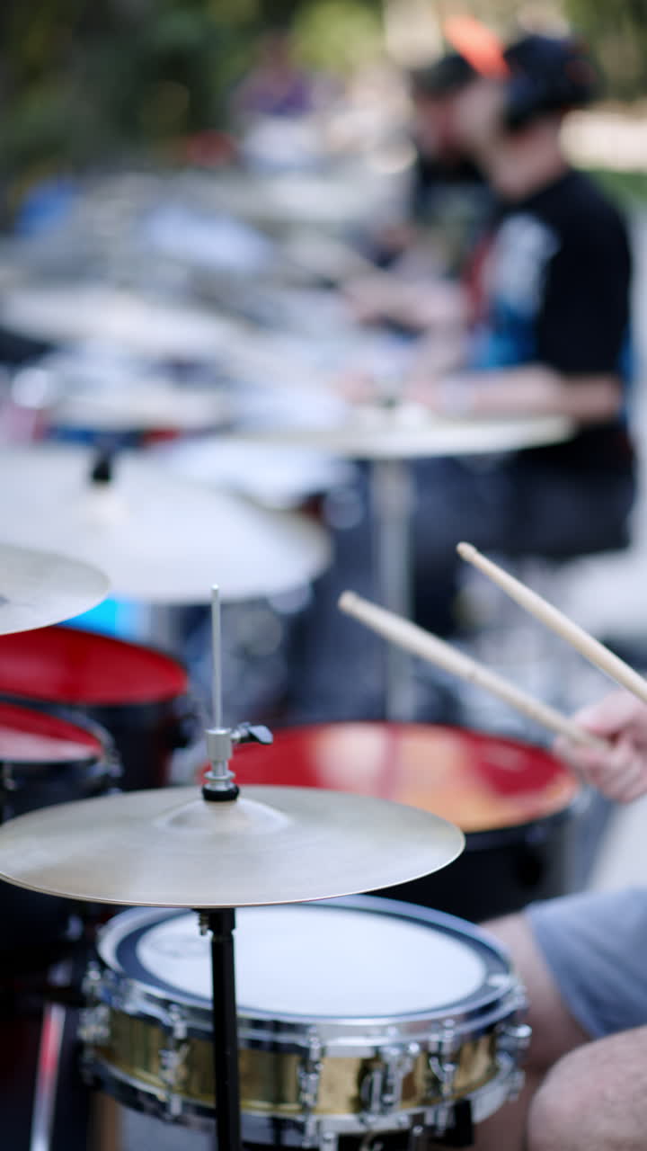 Close up of man playing red drums with a band outside. Vertical