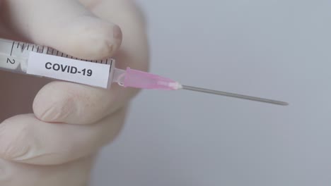 hand wearing medical gloves slowly press syringe to lose bubbles - covid 19 vaccine, close up shot