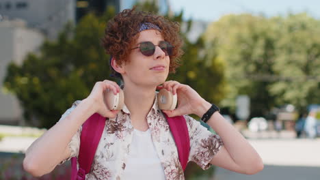 Portrait-of-happy-smiling-tourist-young-man-listening-music-taking-off-headphones-looking-at-camera