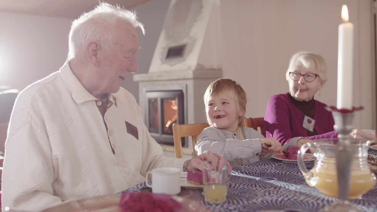 Gap-toothed smiling boy eats tart between great-grandparents at dining table