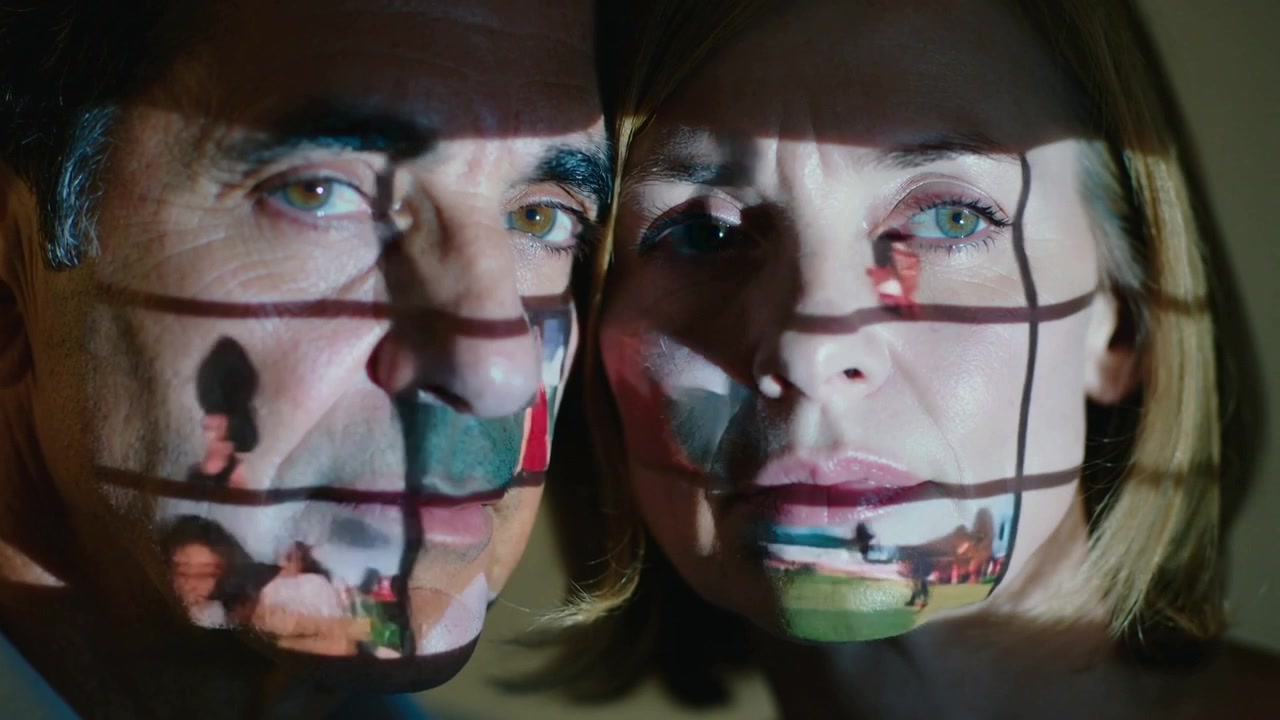 Standing cheek to cheek couple holding still in dim room, projector cycling grid of small images
