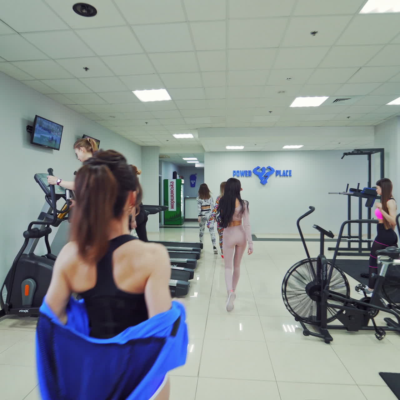 Modern fitness center with various simulators. Back view of athletic young women going out confidently after training of the health club. Camera moves forward.