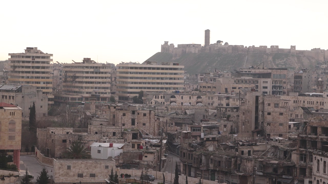 Hazy distant view of the Citadel of Aleppo rising above the city skyline in Syria. Iconic medieval fortress surrounded by the sprawling ancient urban landscape