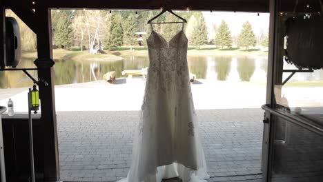 walking out of a rustic wedding venue with a elegant wedding dress hanging just outside the entrance way with a pond and trees in the background at bean town ranch near ottawa canada