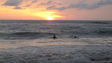 silhouette of two surfers at sunset bobbing up and down waiting for waves