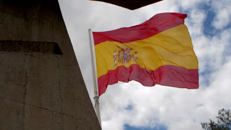 spanish flag waves proudly against a textured concrete structure and a sky filled with light clouds, evoking strength and identity.