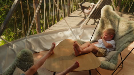 little children relax on shady glamping ground. dreaming little boy with girl sit on chairs with fur coatings under glass sphere. kids at resort