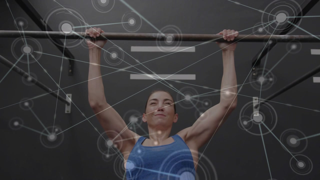 Pulling female athlete wearing blue tank and dark bottoms on metal rig at gym, with HUD