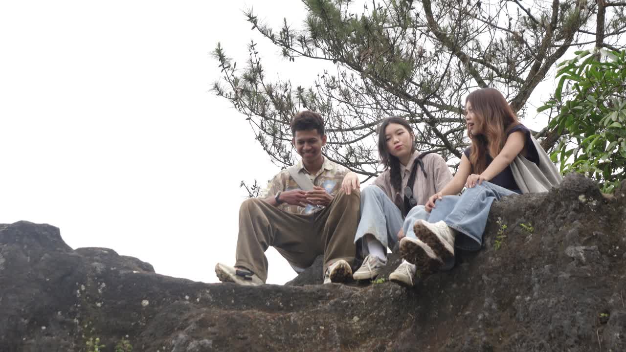 Young Asian Indonesian Friends Chatting and Laughing on Rocky Hilltop in Nature