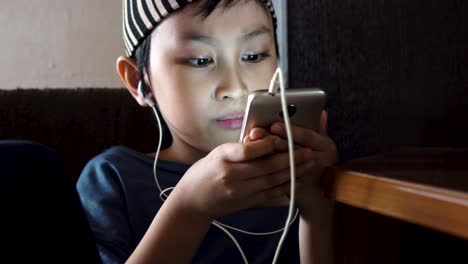 young southeast asian muslim boy watching videos on handphone, alone indoors in dimly lit room