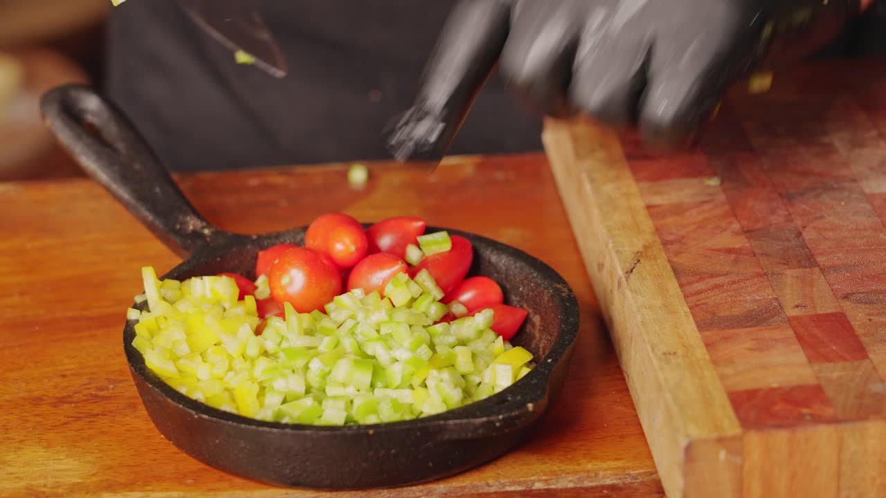preparación de ingredientes para ensaladas, chef profesional con guantes, transfiriendo pimiento verde cortado en cubitos a una sartén de piedra junto a jugoso tomate cherry
