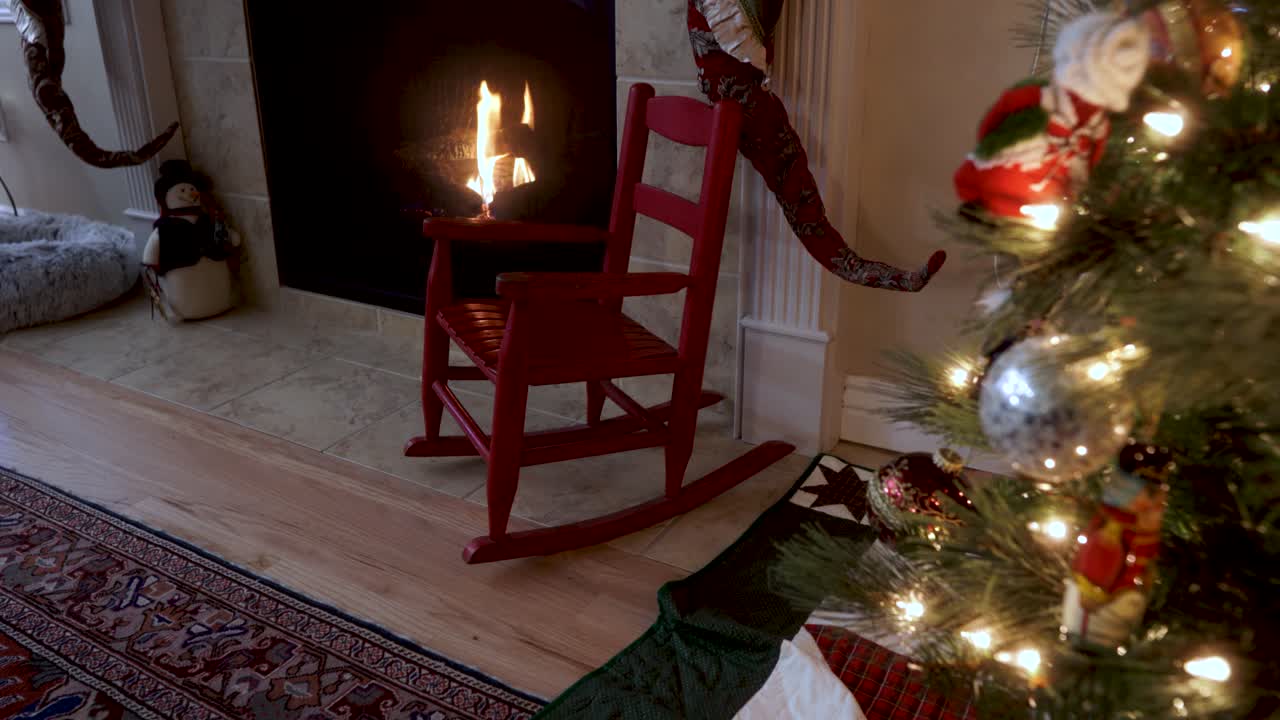 silla mecedora para niños junto a una chimenea y un árbol de navidad decorado con adornos y luces