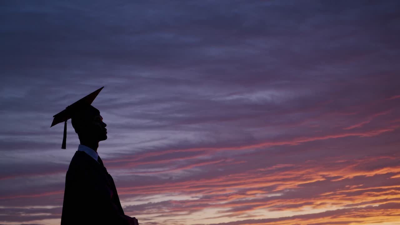 A graduate stands silhouetted against a vibrant sunset, symbolizing new beginnings
