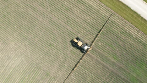 Aerial-top-down,-tractor-with-pesticide-spraying-attached-driving-on-farm-field