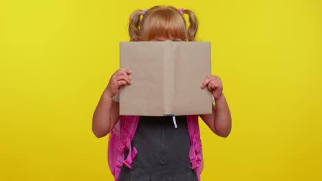 Funny-kid-primary-school-girl-with-ponytails-wearing-uniform-peeping-while-hiding-behind-a-book