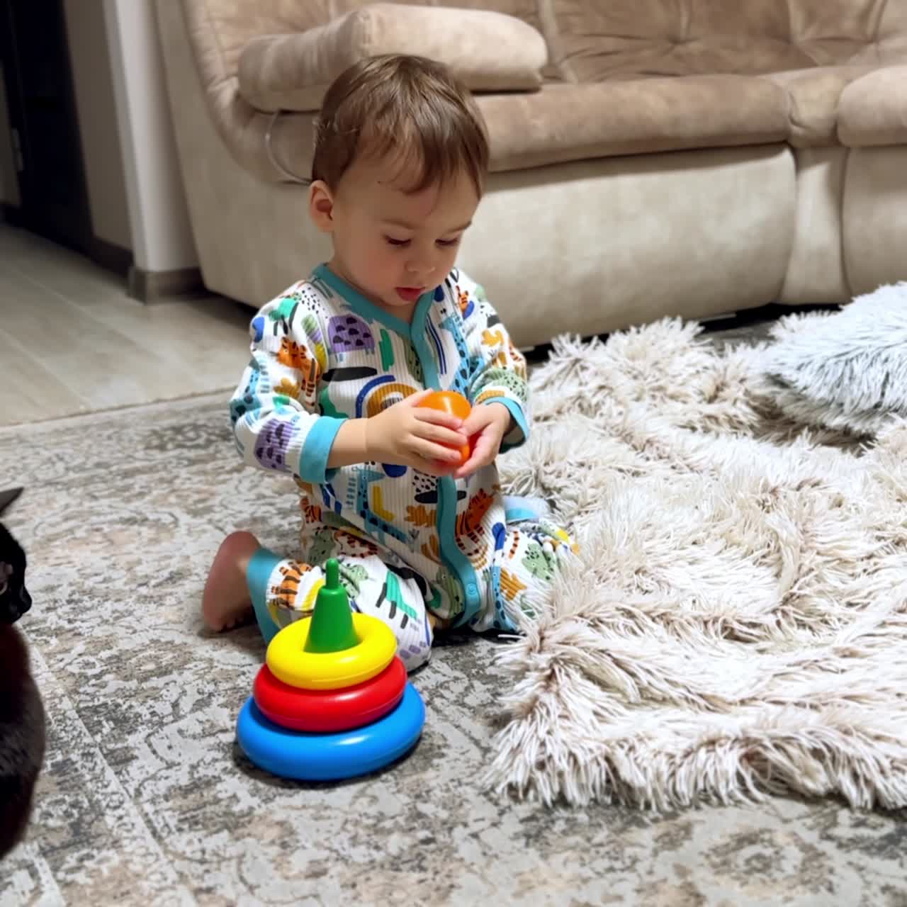 Beautiful Caucasian baby boy in colorful romper sits on the floor. Kid plays with a toy and holds his hand up for something. Vertical video