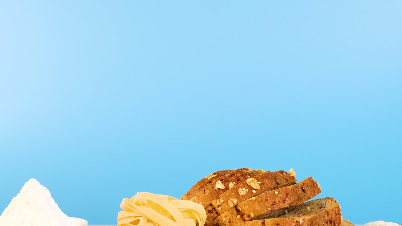 A variety of grains, pasta, and bread displayed on a surface with a bright blue background, highlighting texture and color