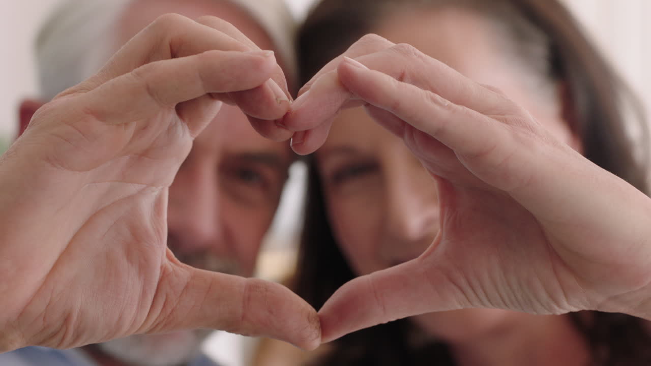 cerca una feliz pareja de ancianos haciendo forma de corazón con las manos gesticulando compromiso romántico disfrutando de una relación amorosa