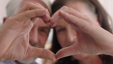cerca una feliz pareja de ancianos haciendo forma de corazón con las manos gesticulando compromiso romántico disfrutando de una relación amorosa