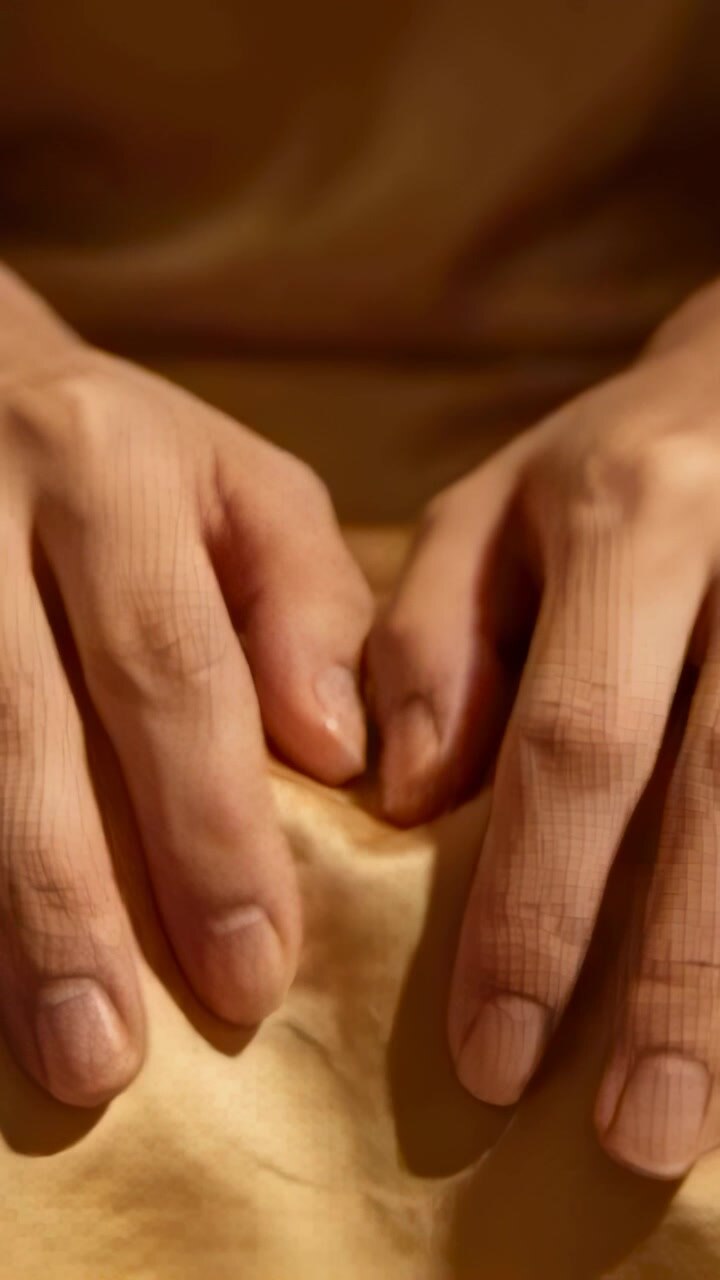 Vidéo verticale : Mains nues pressant après le repos, lissant du satin doré sur les genoux et créant des plis.