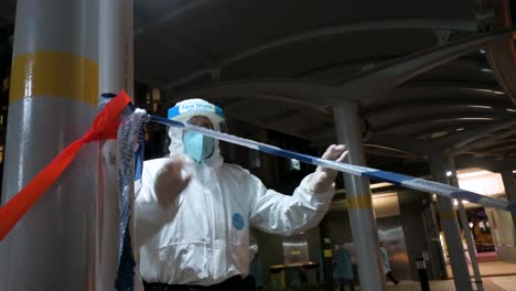 an officer sets up a police cordon tape as he wears a protective suit while a building is under lockdown after a large number of residents tested covid-19 coronavirus positive