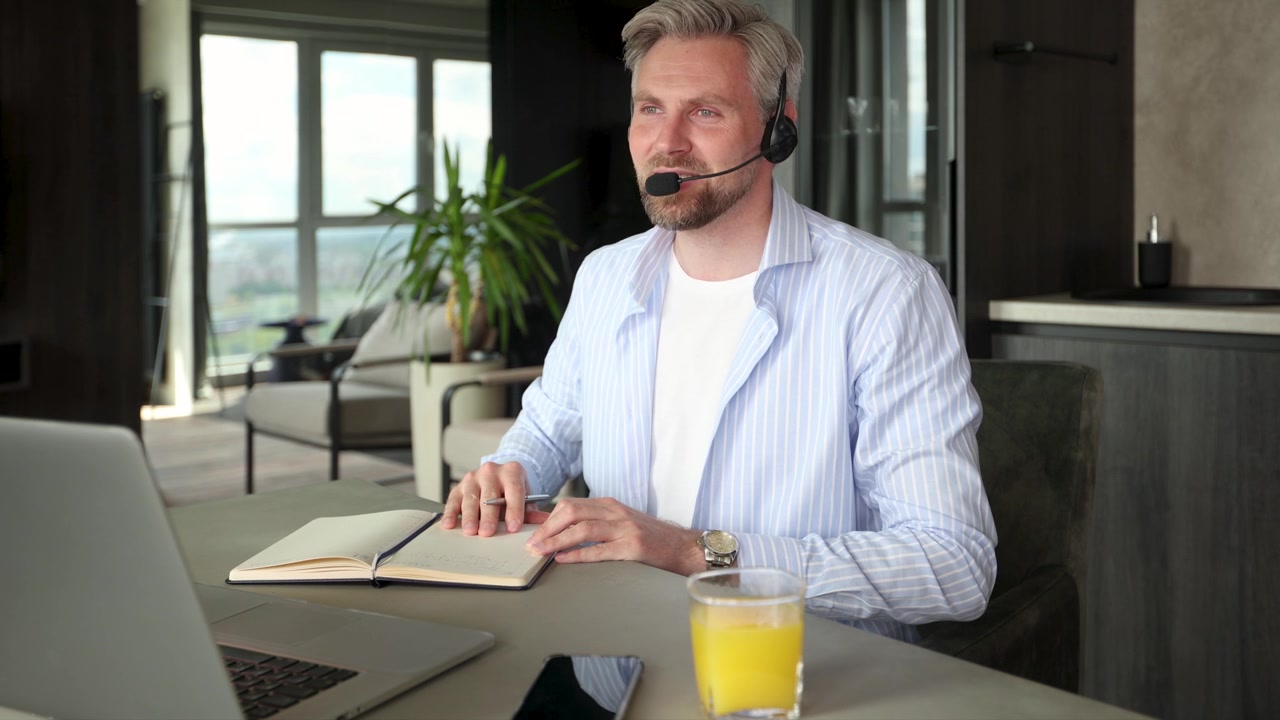 Fokuseret mand med headset arbejder på bærbar computer og tager noter.