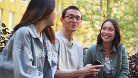 Gruppe-Von-Drei-Jungen-Japanischen-Freunden,-Die-Sich-Unterhalten,-Während-Sie-Draußen-Im-Park-Sitzen-1