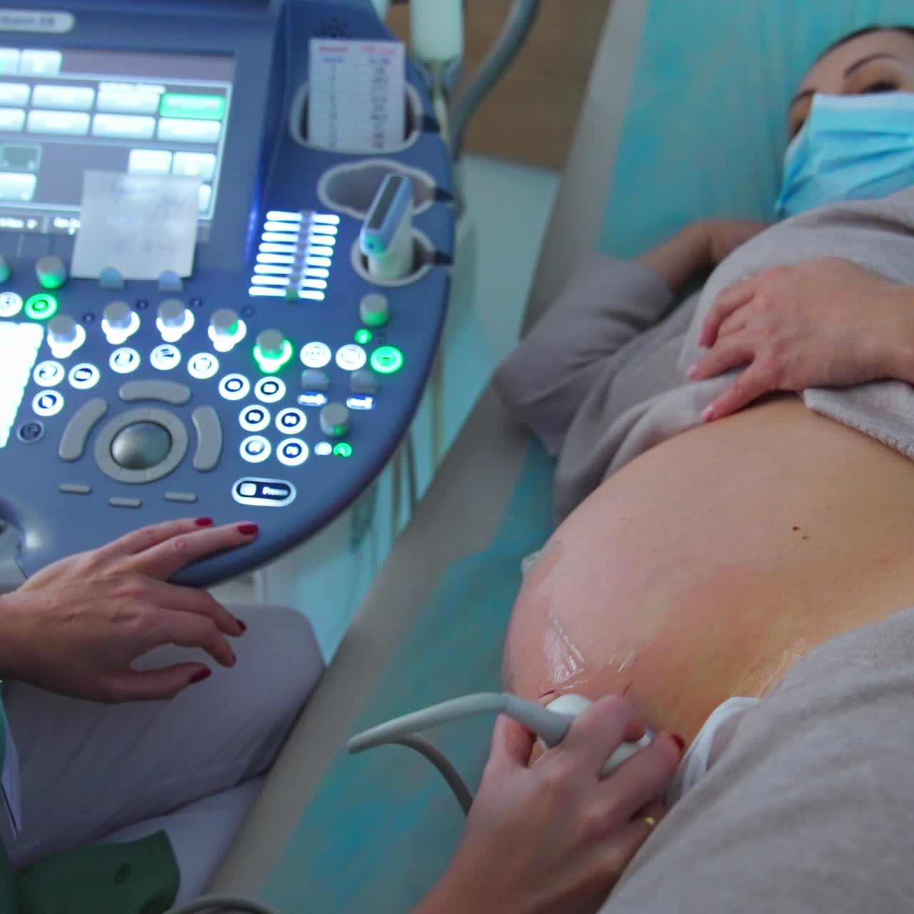Um médico especialista realizando um ultrassom em uma gestante. A paciente está deitada de lado enquanto o médico move o dispositivo em sua barriga.