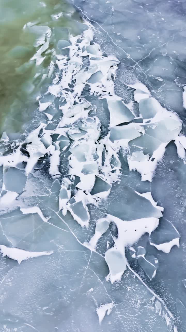 Primer plano de una superficie congelada rota junto a una franja de agua de deshielo verdosa, revelando una frágil y fina capa y peligrosos patrones de fractura — textura abstracta de peligro invernal, vertical.