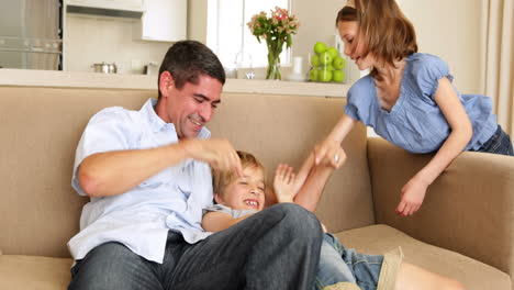 Padre-E-Hija-Haciéndole-Cosquillas-A-Un-Niño-En-El-Sofá