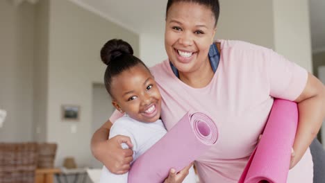 Portrait-of-unaltered-happy-african-american-mother-and-daughter-with-yoga-mats-hugging,-slow-motion