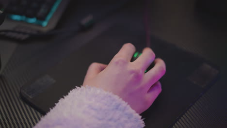 close up of hand wearing fluffy sweater using mouse on dark mouse pad, illuminated by ambient blue and pink lighting, keyboard slightly visible in background