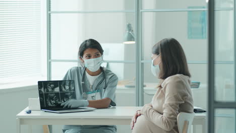 midwife in mask showing ultrasound scan to pregnant woman