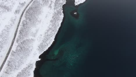 Drone-view-in-Tromso-area-in-winter-flying-over-a-fjord-surrounded-by-white-mountains-top-view-in-Norway