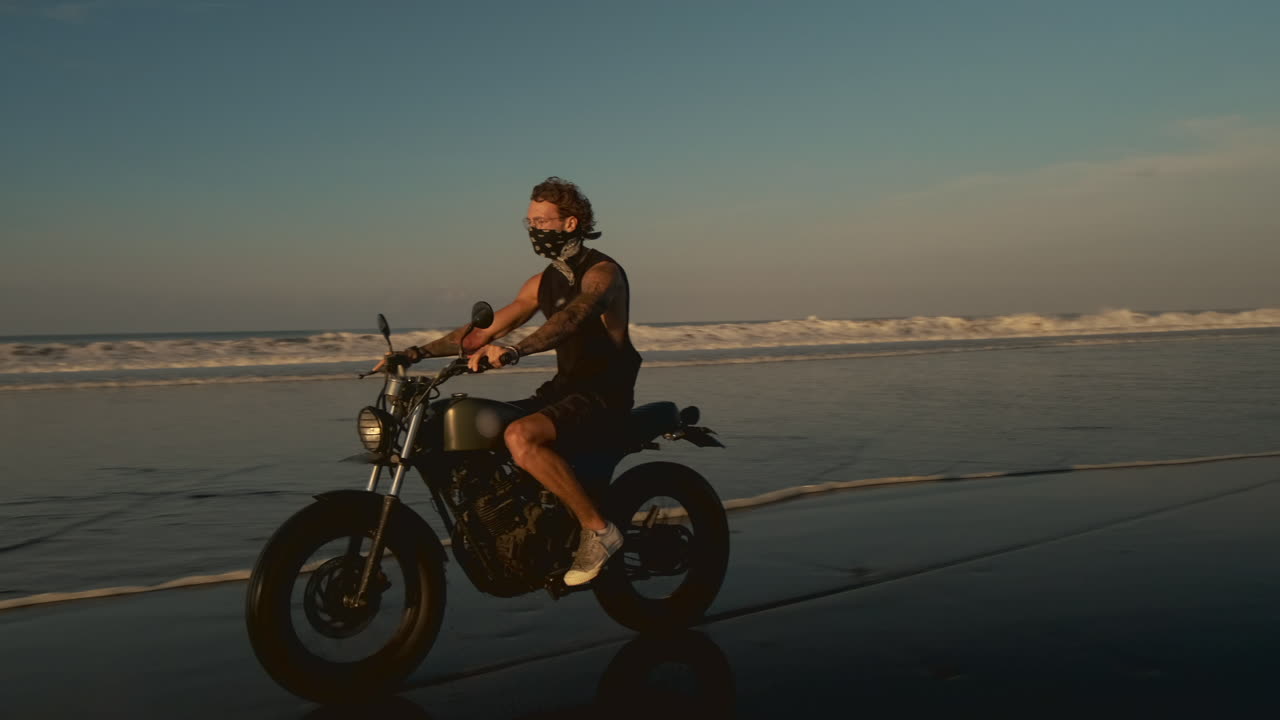 Man Riding a Motorcycle on a Beach at Sunset