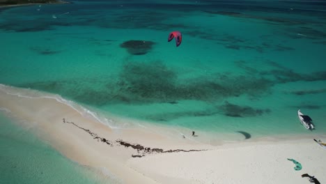 Una-Persona-Practicando-Kitesurf-En-Una-Playa-De-Arena-Con-Aguas-Turquesas,-Vista-Aérea