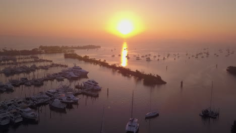 aerial high angle fly over boat filled harbor away from sunrise