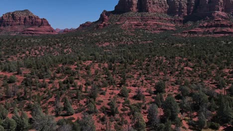 Drone-Aéreo-Volando-Sobre-La-Maleza-Del-Desierto-En-Sedona,-Arizona-Y-Panorámica-Para-Revelar-Formaciones-De-Arenisca-Roja-Con-Vista-De-Punto-De-Pollo-En-La-Distancia