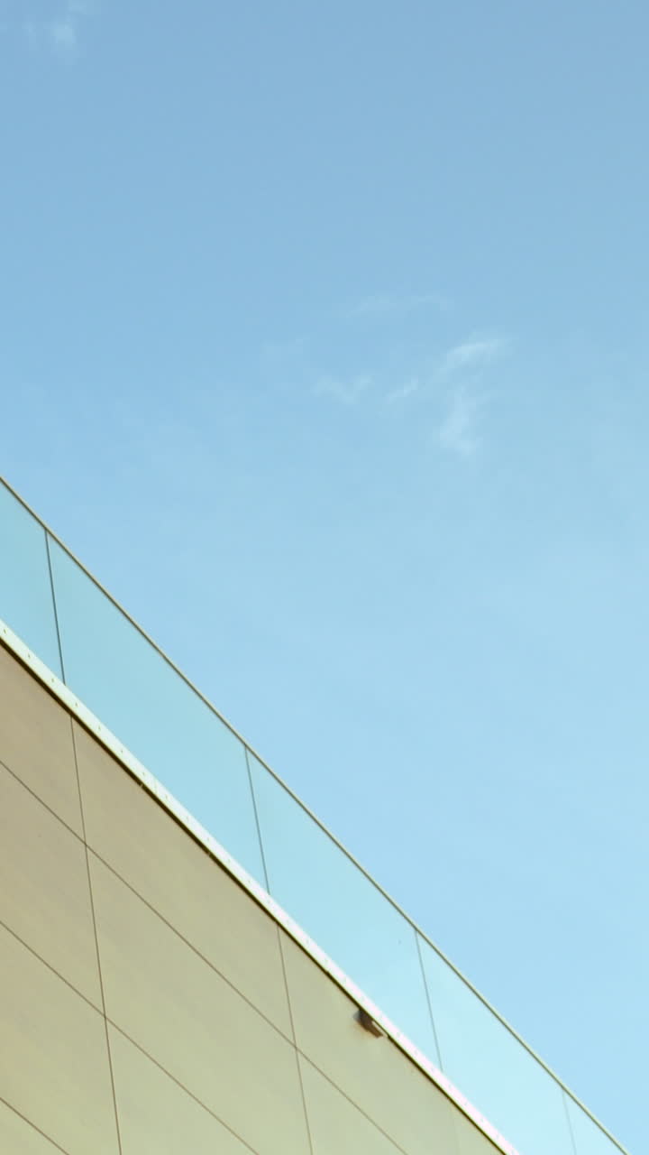 Una ripresa verticale di una facciata di edificio contemporaneo caratterizzata da linee pulite, ringhiere in vetro e un cielo azzurro limpido. Ideale per contenuti di immobili e design urbano.