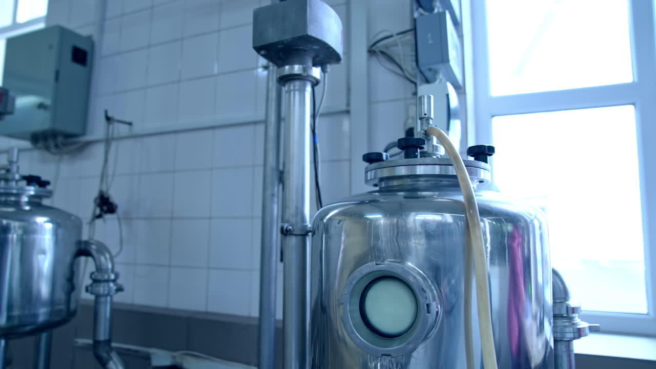 Two small cisterns with the adjusted pipes and tubes. Metal reservoirs placed in front of the window at the milk factory. Close up.
